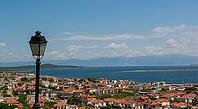 A picturesque seaside town with terracotta rooftops gazes toward tranquil blue waters and distant islands [IBR124920188]