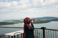 Traveler captures peaceful coastal panorama from terrace overlooking blue water and green islands [IBR124920204]
