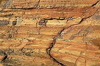 Detailed nature photo of a reddish-brown sandstone formation on a coast. The close-up shows the distinctive texture of horizontal sediment layers formed by centuries of erosion. Embedded in the rocky structure are various smaller, colorful pebbles and tid [IBR124920208]