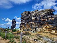 Spectacular view of the historic Devil's Wall in an idyllic heath landscape. The mighty sandstone rock formation fascinates with its rugged structures, earthy tones and a distinctive, free-standing rock needle in the background. A wooden rope fence lines  [IBR124920214]