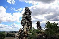 Spectacular view of the historic Devil's Wall in an idyllic heath landscape. The mighty sandstone rock formation fascinates with its rugged structures, earthy tones and a distinctive, free-standing rock needle in the background. A wooden rope fence lines  [IBR124920216]