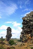 Spectacular view of the historic Devil's Wall in an idyllic heath landscape. The mighty sandstone rock formation fascinates with its rugged structures, earthy tones and a distinctive, free-standing rock needle in the background. A wooden rope fence lines  [IBR124920217]