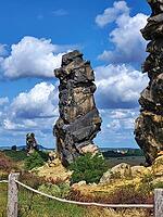 Spectacular view of the historic Devil's Wall in an idyllic heath landscape. The mighty sandstone rock formation fascinates with its rugged structures, earthy tones and a distinctive, free-standing rock needle in the background. A wooden rope fence lines  [IBR124920218]