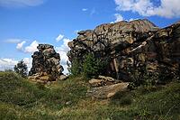 Spectacular view of the historic Devil's Wall in an idyllic heath landscape. The mighty sandstone rock formation fascinates with its rugged structures, earthy tones and a distinctive, free-standing rock needle in the background. A wooden rope fence lines  [IBR124920221]