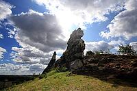 Spectacular view of the historic Devil's Wall in an idyllic heath landscape. The mighty sandstone rock formation fascinates with its rugged structures, earthy tones and a distinctive, free-standing rock needle in the background. A wooden rope fence lines  [IBR124920222]