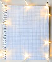 Christmas lights on gray table with notebook, view from above [IBR124944034]