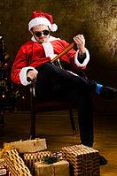 Bad Santa with baseball bat sitting indoors near Christmas or New Year fir tree [IBR124944047]