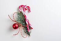 Christmas or new year decoration of two candy cones with fir-tree branch and toy glass ball on gray background [IBR124944080]