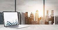 Laptop on table in office with panoramic sunset view of modern downtown skyscrapers at business district [IBR124944113]