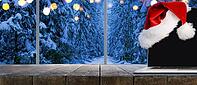 Laptop on table with Santa Claus hat at home with panoramic view through window of snowy trees in winter forest [IBR124944123]