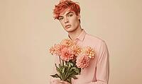 A portrait of a young man with coral-colored hair, holding a bouquet of coral dahlias at his side. AI generated [IBR125000265]