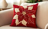 Muted red pillow with ivory poinsettia print and gold stitching details, placed on a pale cream sofa. AI generated [IBR125000269]
