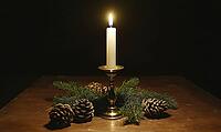 Simple tabletop setup with a brass candlestick and a single white candle, surrounded by small green pinecones. AI generated [IBR125000277]