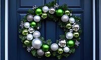 Simple white wreath with silver and green ornaments, hanging on a dark blue door, illuminated by natural daylight. AI generated [IBR125000278]