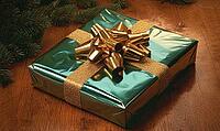 Close-up of a neatly wrapped gift with a golden bow on a wooden table. AI generated [IBR125000301]