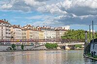 The red footbridge Passerelle Saint-Vincent spans the river Saone, bounded on the left by the portal of the Eglise Notre-Dame-Saint-Vincent de Lyon and the house facades on the Quai de la Pecherie under a dramatic cloudy sky in Lyon, Metropole de Lyon, Rh [IBR125002335]