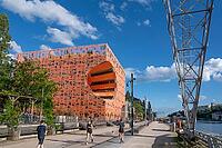 Modern architecture meets industrial history on the banks of the Saone river with the distinctive Le Cube Orange building by architects Jakob and MacFarlane on the Quai Rambaud waterfront with passers-by and a historic crane structure under a blue sky in  [IBR125002338]