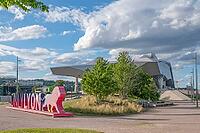 Colourful OnlyLyon marketing sculpture with lion figure as the city's landmark against the futuristic backdrop of the Musee des Confluences by Coop Himmelblau, surrounded by green trees and white clouds in the blue sky in Lyon La Confluence, Rhone, Auverg [IBR125002339]
