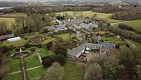 Aerial view of a countryside estate with multiple buildings surrounded by gardens and trees under an overcast sky, Farm in Wales, United Kingdom [IBR125026136]