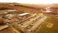 Aerial view of a rural area with buildings, a parking lot, and fields during sunset, Tesla charging station near Exeter, Devon, UK [IBR125026139]