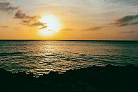 A tranquil sunset over a calm ocean, with orange and yellow hues reflecting on the water, aruba [IBR125026141]