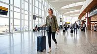 A cheerful woman with a boarding pass and luggage navigates a busy airport concourse, ready for her flight, AI generated [IBR125026409]