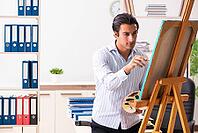 Young handsome employee enjoying painting at the office [IBR125053199]