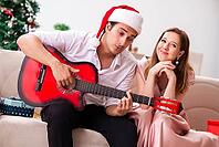 Young couple playing guitar at christmas [IBR125053257]