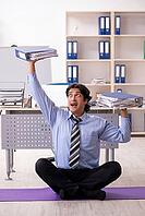 Young handsome male employee doing exercises in the office [IBR125117995]
