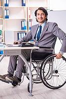 Young handsome employee in wheelchair at the office [IBR125118048]