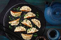 Gyoza, on a black stone platter, with a tetsubin teapot, a bowl with soy sauce, on a wooden table, dark style, no people [IBR125163377]