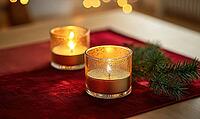 Two glass candle holders with golden candles, placed on a red velvet table runner with a small pine branch nearby. AI generated [IBR125167396]
