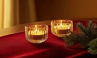 Two glass candle holders with golden candles, placed on a red velvet table runner with a small pine branch nearby. AI generated [IBR125167399]