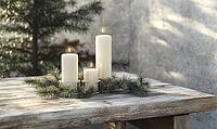 Simple wooden table with a trio of white candles in glass holders, scattered pine branches around the base. AI generated [IBR125167416]