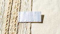 White woven garment care label lying on blended ivory fabric, raking light revealing two distinct thread types in fabric weave below, textile fiber mislabeling and authenticity concept, studio shot, AI generated [IBR125167440]