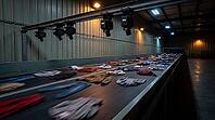 Industrial textile sorting facility conveyor belt with blurred mixed donated clothing in motion, NIR sensor and camera arrays mounted overhead on steel rail, automated fiber identification and recycling concept, no people, studio shot, AI generated [IBR125167442]