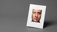Passport-format identity photograph card showing morphed composite face, two different faces joined at vertical centerline, face morphing identity fraud concept, grey background, studio shot, AI generated [IBR125167460]
