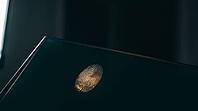 Latent fingerprint friction ridge detail revealed by raking sidelight on dark glass surface, amber luminous ridge lines against teal-black background, forensic crime scene investigation concept, studio shot, AI generated [IBR125167463]
