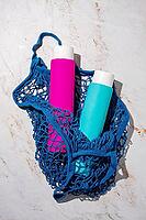 A net bag holds two bottles. One bottle is pink and the other is blue. The scene shows a light-colored surface underneath the bag [IBR125177931]