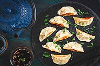 Gyoza, on a black stone platter, with a tetsubin teapot, a bowl with soy sauce, on a wooden table, dark style, no people [IBR125178016]