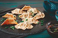 Gyoza, on a black stone platter, with a tetsubin teapot, a bowl with soy sauce, on a wooden table, dark style, no people [IBR125178017]