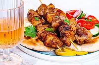 Souvlaki, a Greek dish, grilled meat shish kebab, on a plate with flatbreads, and lemon slices, grilled meat shish kebab, served with lavash, salad and drinks where there are no people [IBR125178019]