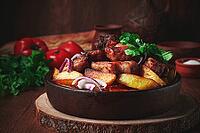 Ojakhuri, fried meat with potatoes, in ketsi, on a wooden table, Georgian cuisine, against a background of fresh ingredients [IBR125178020]