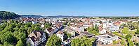 A wide-angle panorama from the air shows the city of Homburg on a sunny day. Residential buildings and trees are in the foreground, while the city center with streets and shops runs through the middle. In the background, wooded hills and the distinctive S [IBR125180379]