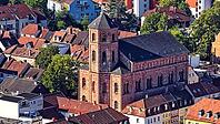 The close-up from the air shows the distinctive Lutheran town church in Homburg. The reddish sandstone architecture of the religious building with the distinctive church tower and the tower clock is in focus. Densely lined residential buildings with red t [IBR125180381]