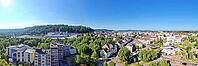 A wide-angle panorama from the air shows the city of Homburg on a sunny day. Residential buildings and trees are in the foreground, while the city center with streets and shops runs through the middle. In the background, wooded hills and the distinctive S [IBR125180382]