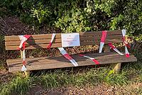 Blocked park bench with warning sign and barrier tape in sunlight, Guxhagen, Hesse, Germany [IBR125180393]