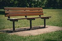 Wooden park bench on a concrete pad surrounded by grass in a park. abstract concepts of pause, waiting period, quiet contemplation [IBR125185825]