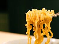 Close-up of ramen or noodles being lifted by a fork against a dark background [IBR125185843]