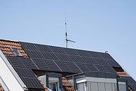 A residential building roof with solar panels. Clear blue sky with sunshine guarantees high electricity production. Dormer Windows and Skylights Provide More Light in the Attic Apartments [IBR125185851]